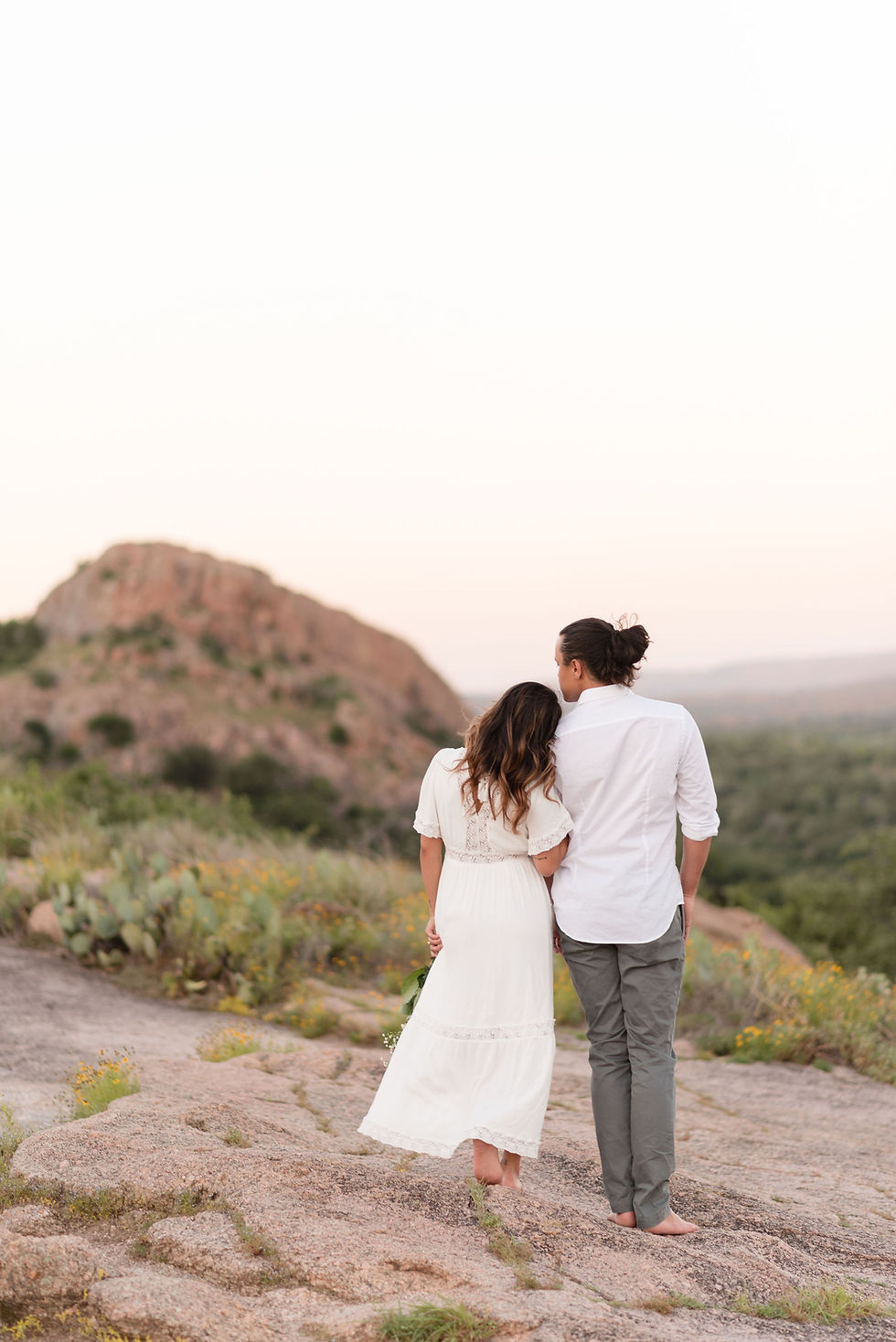 bride and groom have their backs to the camera, looking out at the view of enchanted rock. bride has her head resting on grooms shoulder
