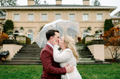 couple under single umbrella after elopement kissing in the rain