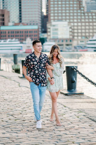 couple walking along harborwalk in boston seaport for engagement session