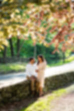 couple poses together sitting on stone wall underneath a tree