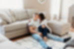 in home engagement session couple sits on floor next to couch with legs intertwined