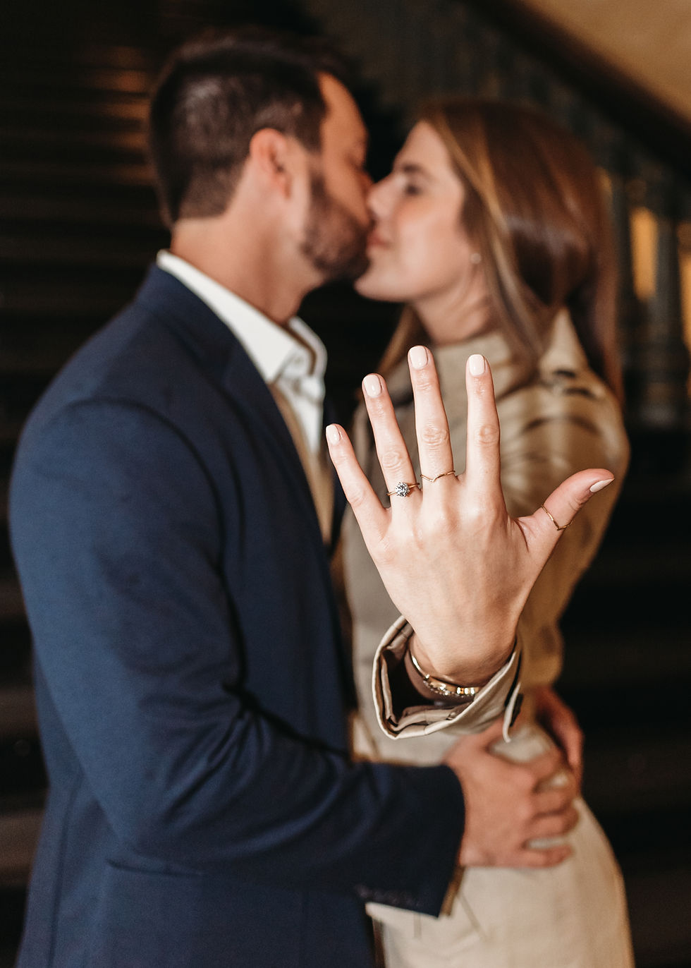 newly engaged couple showing the engagement ring to the camera while kissing