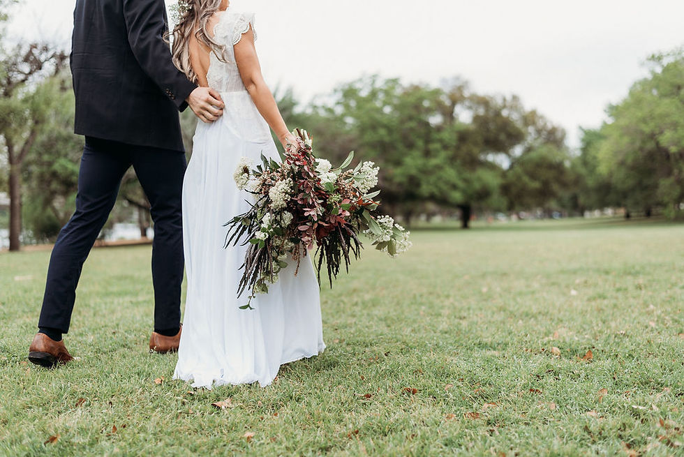 bride and groom hold hands and are walking away from the camera. bride hangs her bridal bouquet down to her side. They are small in the frame and you can see the field behind them. Austin elopement at festival beach next to lady bird lake. you cannot see their faces. the top of the photo cuts off at their shoulders.