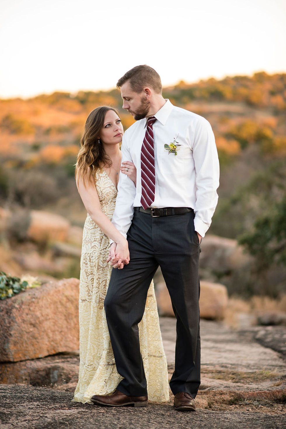 newlyweds pose for photo during enchanted rock elopement. Groom is standing slightly in front of bride with one foot raised. The bride is holding his hand with one arm and the other is wrapped around the groom's bicep. They look at each other seriously