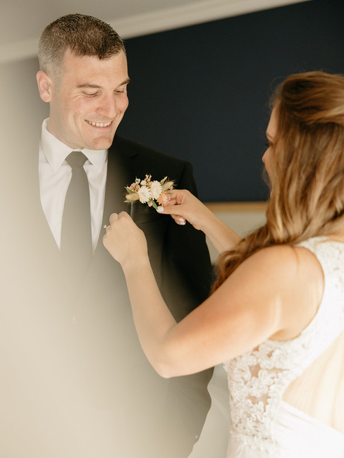 bride putting boutonniere on groom 