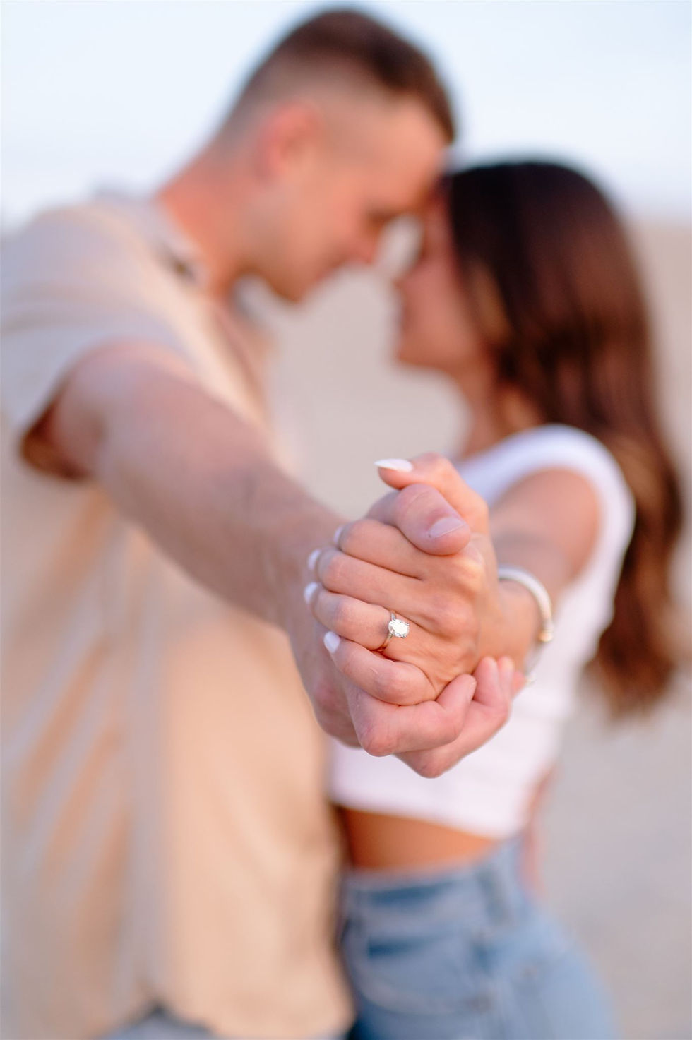 girl and guy holding faces close together with hands extended close to camera to focus on engagement ring