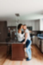 in home engagement session girl sits on kitchen counter with guy standing between legs