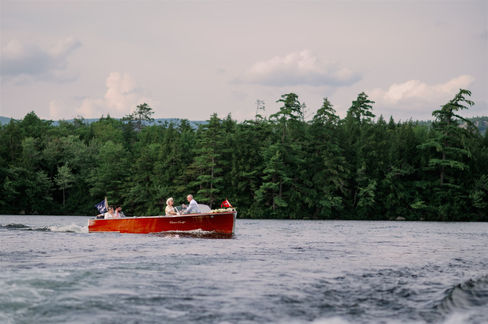 newlyweds on a boat to travel to wedding reception at squam lake inn in holderness, nh