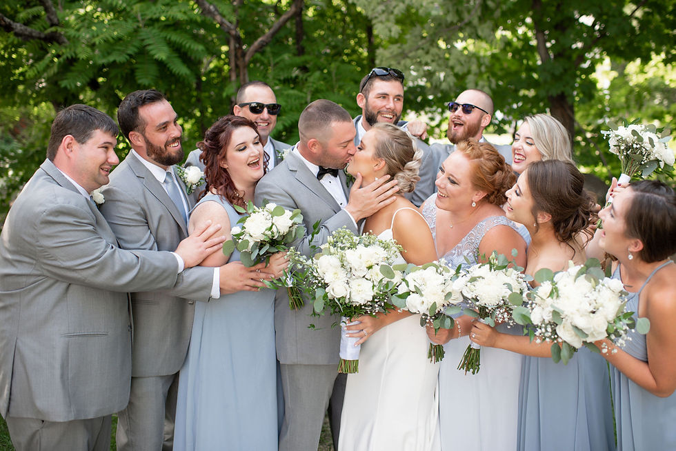 fun wedding party picture everyone laughing while bride and groom kiss
