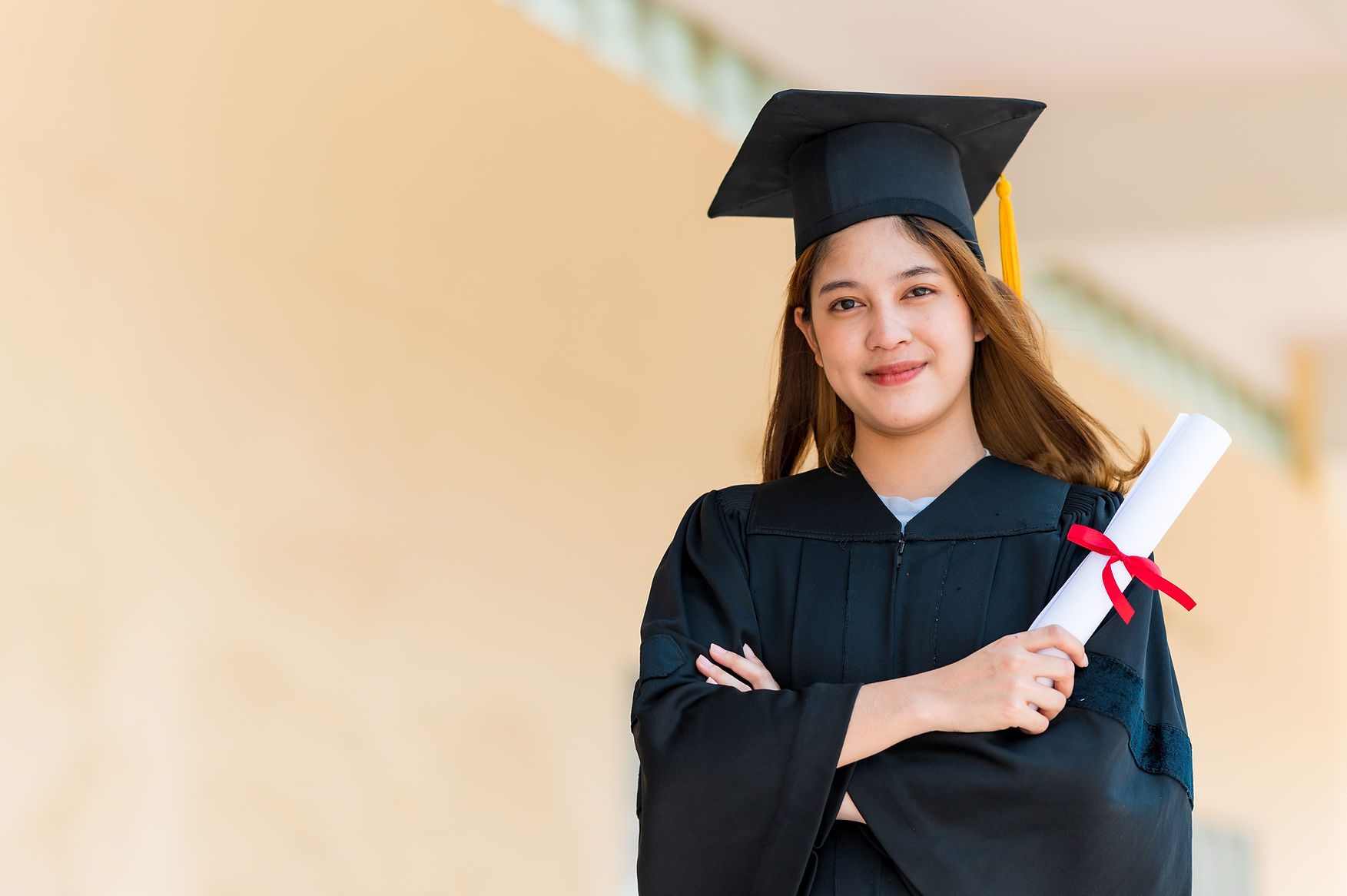 Smiling female Asian student in academic gown and graduation cap holding diploma.jpg