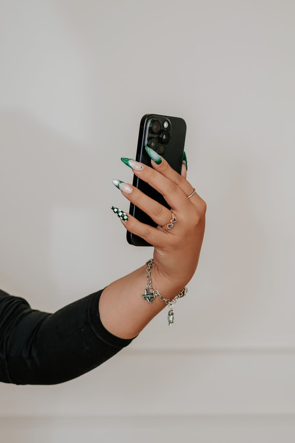 A close-up shot of a person holding a smartphone, showcasing manicured nails with a green-and-white checkered design.