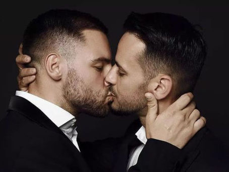 Couple gay élégant en costume qui s’embrasse avec tendresse, image illustrant l’amour entre hommes, le désir dans le couple et l’inspiration du tantra pour raviver la relation et la sexualité consciente.