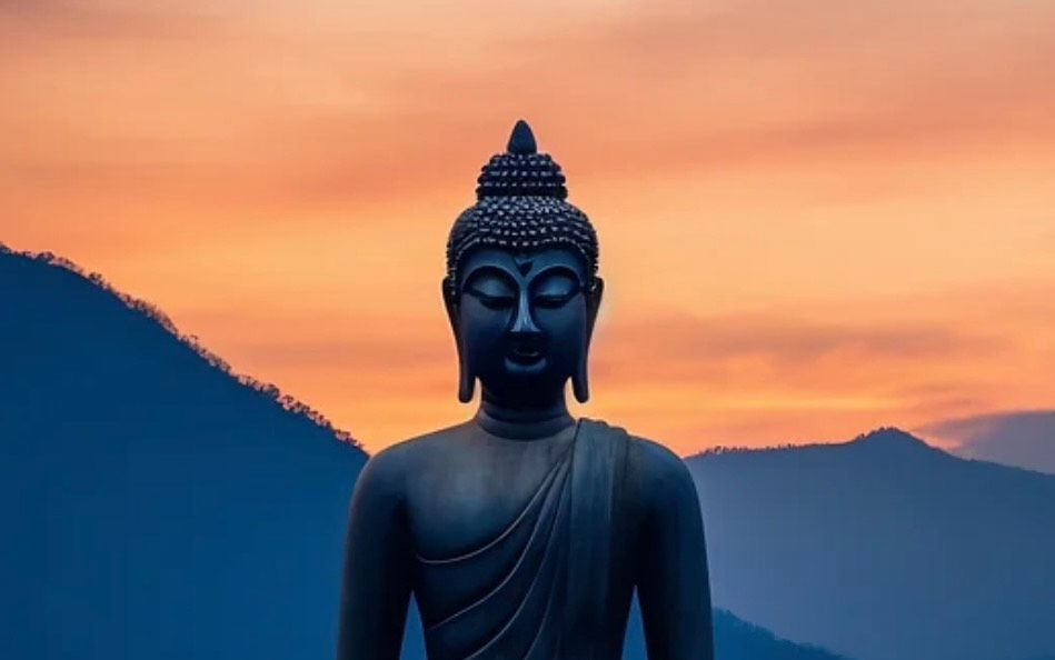 Statue de Bouddha en méditation, assise sur un lotus au milieu de l’eau, baignée par la lumière douce d’un ciel au coucher du soleil. Une image symbolique de paix intérieure, de présence consciente et de spiritualité tantrique, invitant à explorer les différentes voies et couleurs du Tantra.