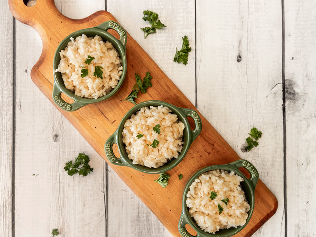 Three small green dishes of cooked long grain white rice with parsley on a wooden board.