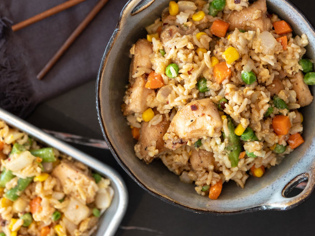 A bowl of chicken fried rice with peas, carrots, and corn beside a sheet pan of the same.