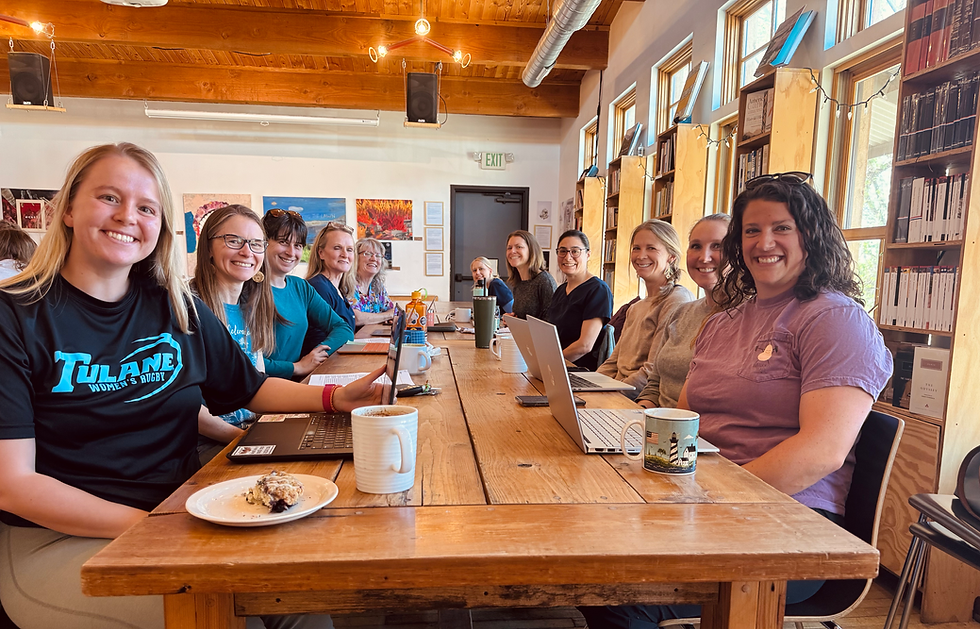 Team of veterinary professionals gathered around a wooden table at a cozy café for journal club, smiling with laptops, coffee mugs, and notes during a collaborative discussion.