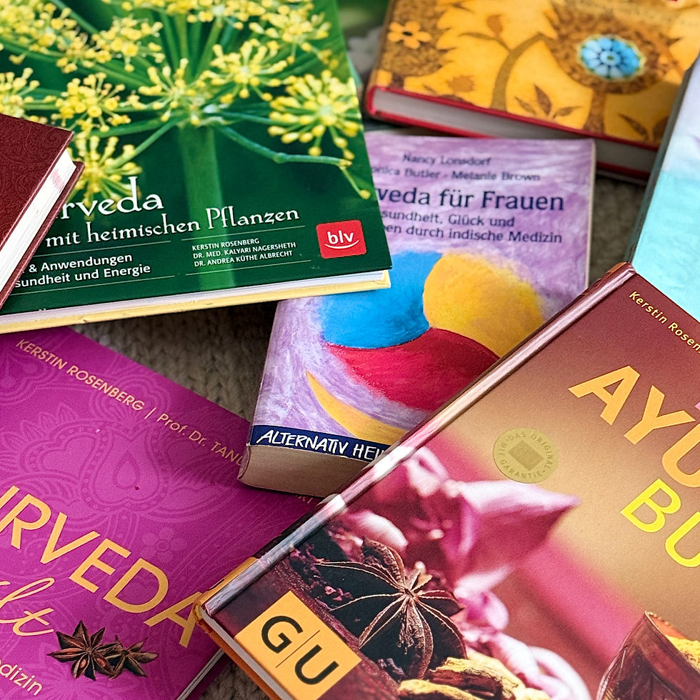 Mehrere Ayurveda-Bücher mit bunten Covern liegen auf einem Tisch; sichtbare deutsche Titel, ruhige Wellness-/Naturstimmung.