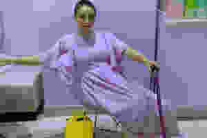 A photo of Elce seated in a wire chair. They're dressed in all purple and holding a sparkling purple cane.