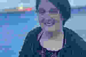 A photo of Alisha. She is looking into the camera and smiling, and has short brown hair and silver glasses.