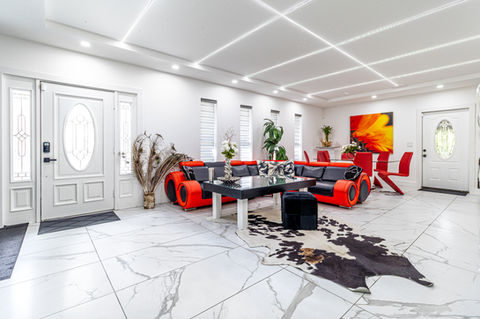 Professional real estate photo of a modern living room with white tile floors, red seating, and front entry doors.