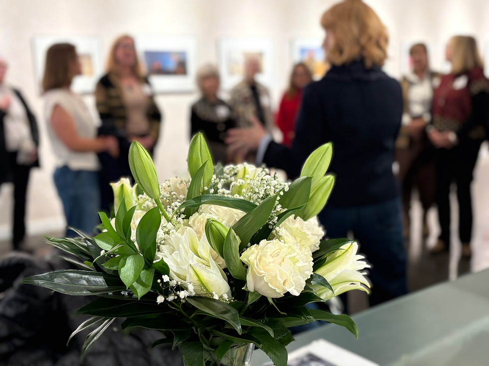 Color photo of a crowd listening to a presenter with a floral arrangement in the foreground