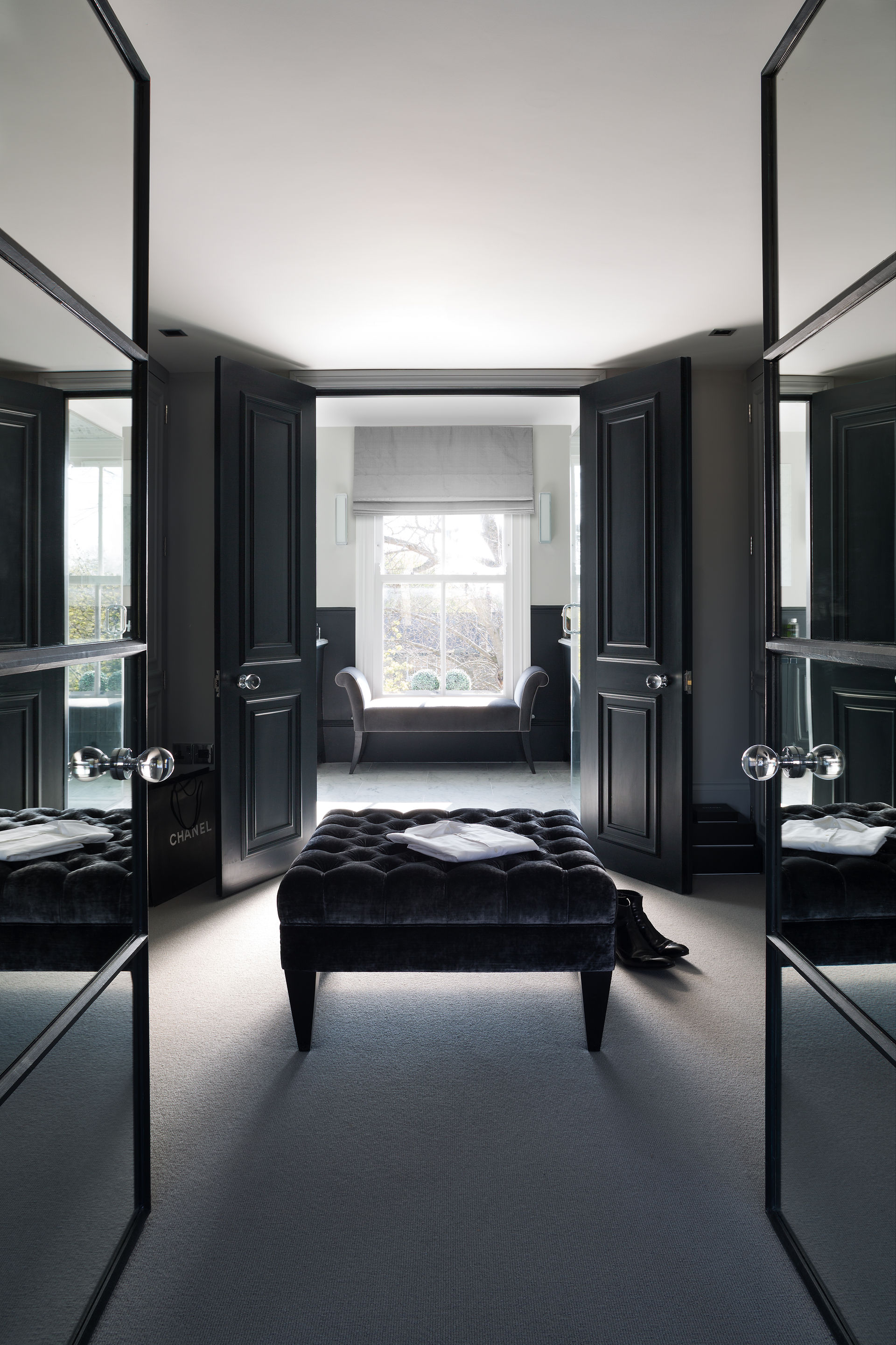 Tailored dressing area with mirrored wardrobes, dark joinery, and a central tufted bench leading into the bathroom.