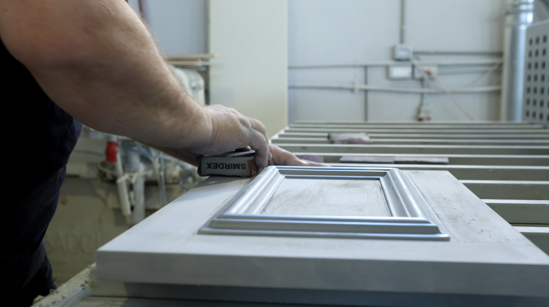 Hand sanding a detailed cabinet door edge in workshop
