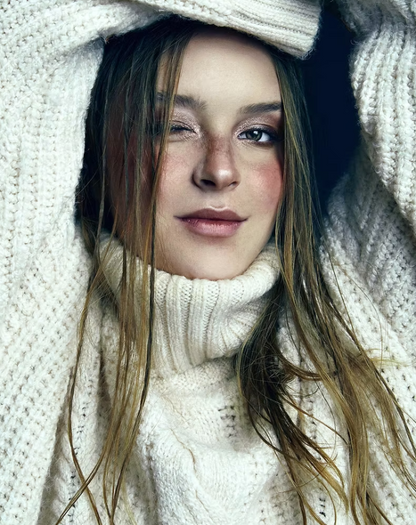 Close-up of a model wearing a white knitted jersey with brown eyes, pulling a silly face