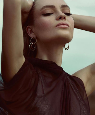 Studio shot of a young woman standing confidently against a light green background holding her hair back