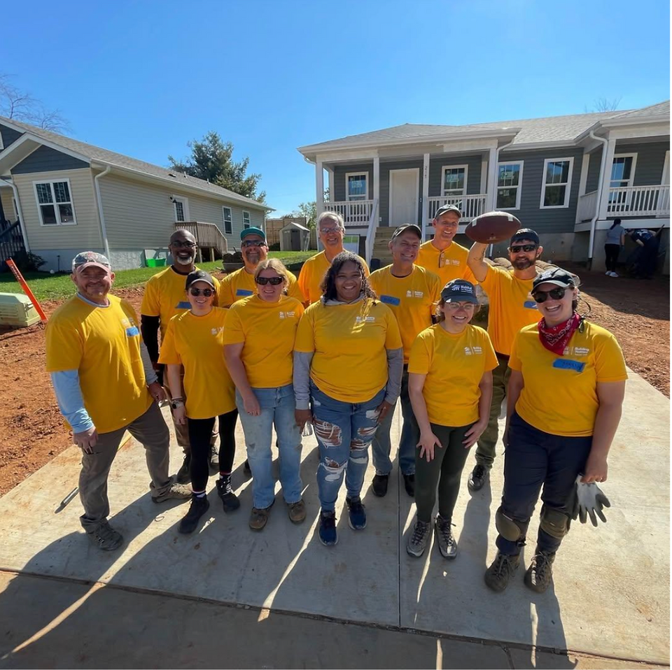a group of smiling volunteers in yellow in front of a house. 
