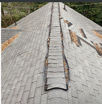 The ridgeline of a damaged shingled roof shows stains, debris and missing shingles.