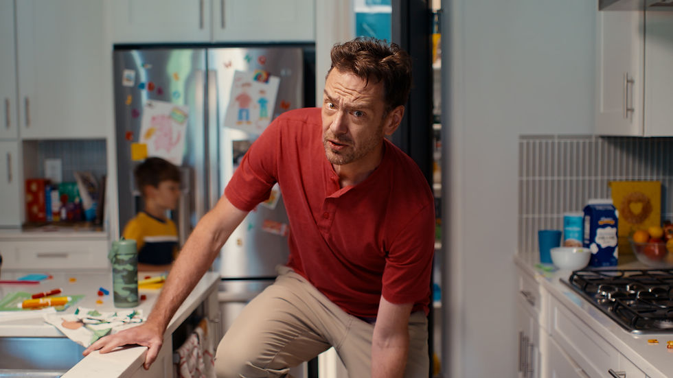 Father reacts to his son during a warm, humorous family kitchen scene.