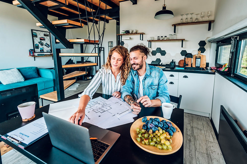 A couple planning their modern farmhouse-style custom home design with blueprints and a laptop in a contemporary kitchen, showcasing the process of building a custom home with Jacob's Construction.