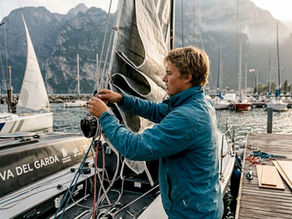 Un giovane skipper si dedica ai preparativi della sua barca a vela sulle rive del Garda, pronto a salpare per una nuova avventura.