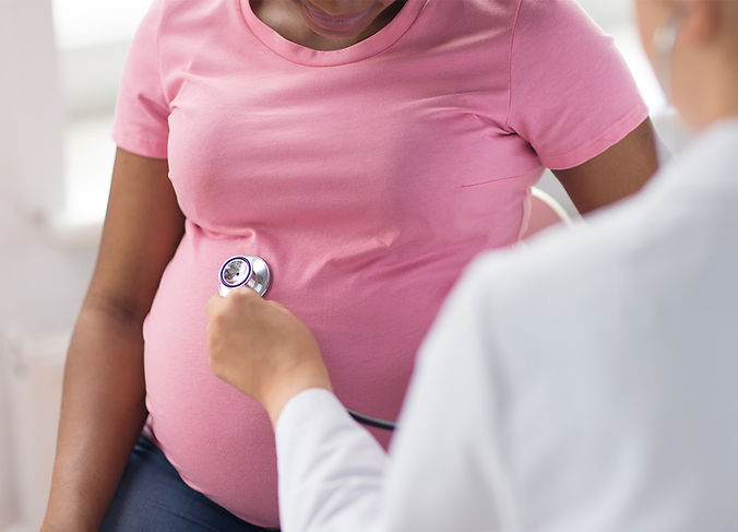Pregnant women in pink shirt with stethoscope on stomach while doctor listens
