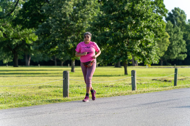 Running Strong member running in a pink shirt during a race at park.