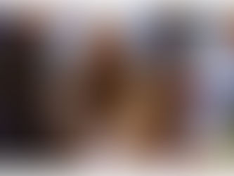 Two people in winter clothing smiling at a holiday market stall with colorful ornaments. Festive lights and snow in the background.