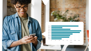 Smiling person with glasses using a phone displaying the Driftscape digital tourism app showing a bar chart with dates and content views. Brick wall and plants in background. Casual mood.
