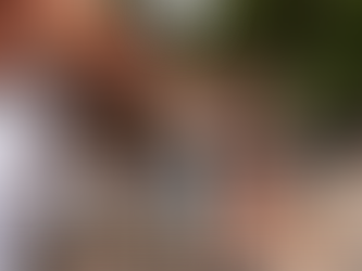 Two women in dresses walk and chat at an outdoor market under orange canopies. A man browses clothes. The mood is relaxed and sunny.