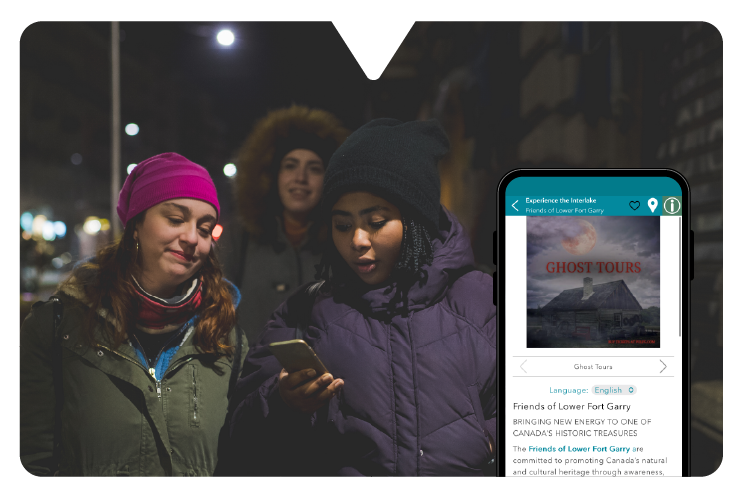 Three people in winter clothing walk at night, one using a smartphone showing the Driftscape walking tour audio app featuring "GHOST TOURS."