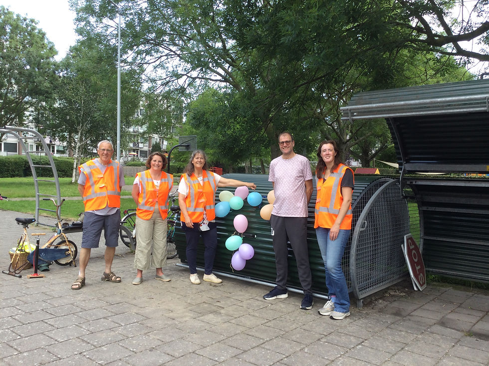 Five people in orange vests smiling beside a bike locker with balloons. 