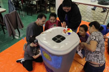 Adults & kids paint a rain barrel.