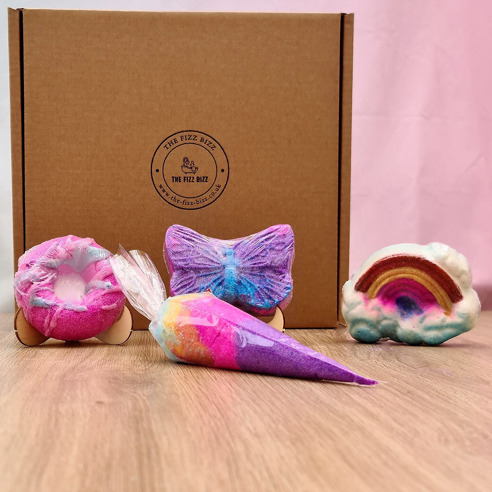 A Butterfly, Rainbow and Pink Donut shaped bath bomb with a rainbow bath dust displayed in front of their included gift box