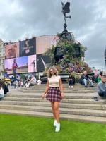 Full body photo of Rasha in a plaid skirt and white boots in London