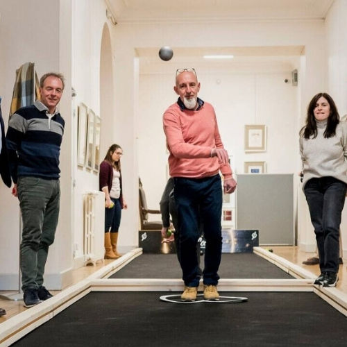 Une homme lance une boule lors d'un Team building pétanque sur des terrains de pétanque synthétiques dans une salle de réunion