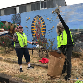 Volunteers removing invasive vegetation in front of a brightly painted and mosaic mural at Jingletown Garden.