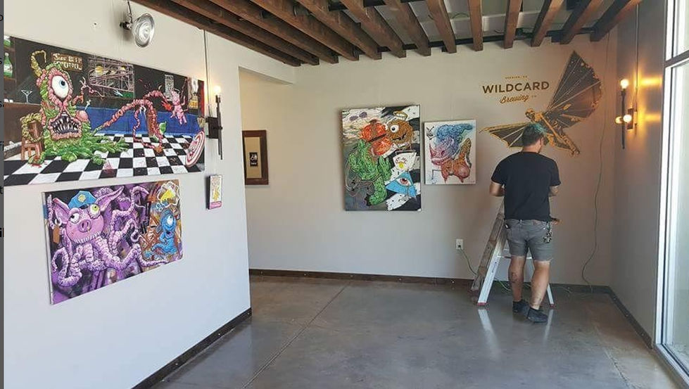 many paintings in art gallery hanging on wall while person installs the paintings