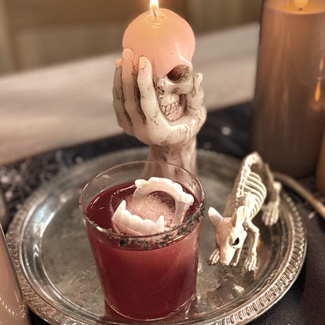 A Dracula's Kiss cocktail sitting on a silver tray in front of a skull candle and next to a rat skeleton for Halloween.