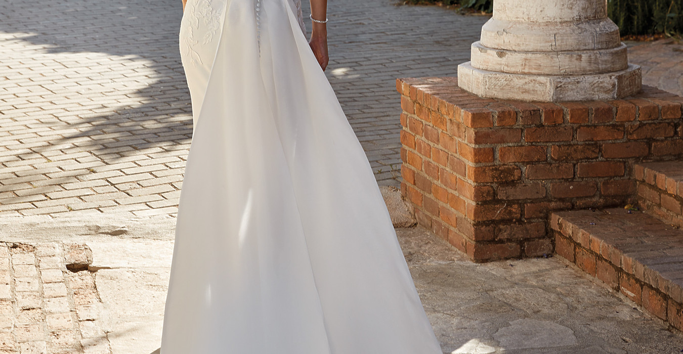 Back of Eddy K Crepe mermaid wedding gown with split train on blonde model with pony tail.