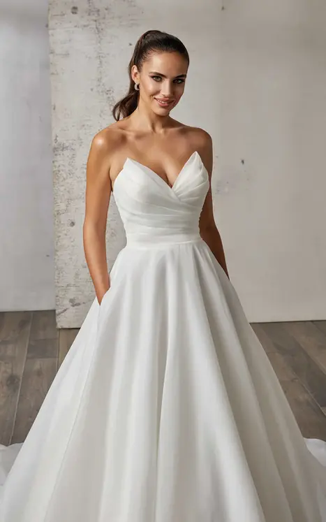 Close up of Eddy K organza ballgown in ivory with cat-eye neckline on bridal model standing in studio.